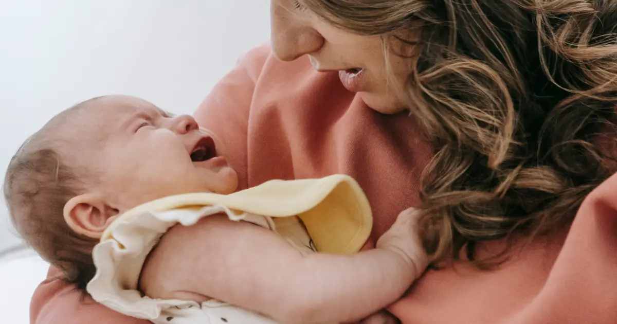 Madre che tiene in braccio un neonato che piange in un momento di interazione e accudimento.